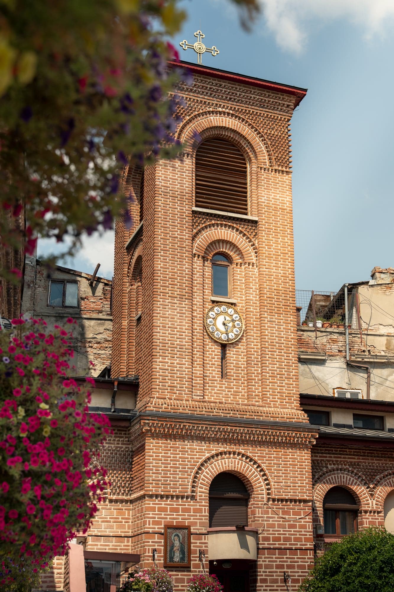 A brick bell tower with flowers in the foreground
